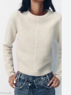 Vit stickad tröja med rund hals - Snygg vit stickad tröja med rund halsringning och lång ärm. Tröjan har en unik söm framtill som ger en modern touch. Perfekt att matcha med jeans för en clean och stilren look. Materialet ser mjukt och bekvämt ut.
