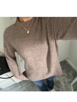 Brun stickad tröja med rund hals - Mysig brun stickad tröja med rund hals och långa ärmar. Tröjan har en enkel, rak passform och ribbstickade muddar vid ärmslut och nederkant. Perfekt att matcha med jeans för en avslappnad look.