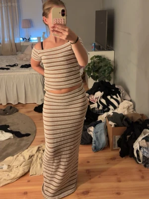 Beige och vit ribbad body set Nelly  - Säljer ett ribbat set med body och lång kjol i beige och vitt. Toppen har off shoulder-modell och korta ärmar, medan kjolen är hellång och figurnära. Materialet är stickat och stretchigt, vilket ger en skön och trendig look. Perfekt för dig som gillar en avslappnad men snygg stil. De finns ett litet hål i kjolen men de är inget jag har lagt märke tills alls och den syns inte🫰🏼