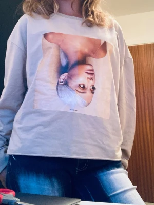 Beige Ariana Grande sweatshirt  - Säljer en beige sweatshirt med ett stort Ariana Grande tryck på framsidan. Tröjan har avslappnad passform, rund halsringning och långa ärmar. Perfekt för dig som gillar statement-plagg och vill ha en unik look.
