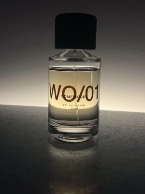 Zara Somewoody WO/01 Eau de Parfum - En stilren parfymflaska i genomskinligt glas med svart lock från Zara. Doften heter Somewood WO/01 och är en Eau de Parfum. Flaskan har en modern, minimalistisk design med tydlig text på framsidan och rymmer 100 ml. Se bild för mängd kvar.