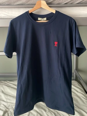 Mörkblå t-shirt med rött hjärta - Snygg mörkblå t-shirt med ett litet rött hjärta broderat på bröstet. Klassisk rund halsringning och korta ärmar. Tillverkad i mjuk bomull som känns skön mot huden. Perfekt för en clean och stilren look.