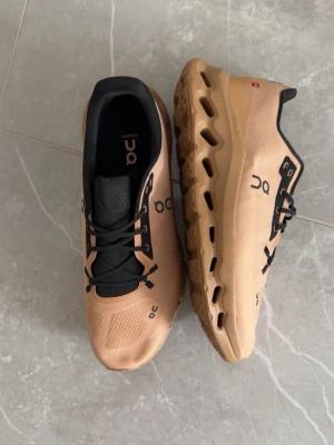 Beige On Running sneakers - Snygga sneakers från On Running i beige med svarta detaljer och logga på sidan. Ovandelen är i mesh för bra ventilation och sulan har On's unika CloudTec-design för extra komfort. Skorna har svarta snören och en sportig look.