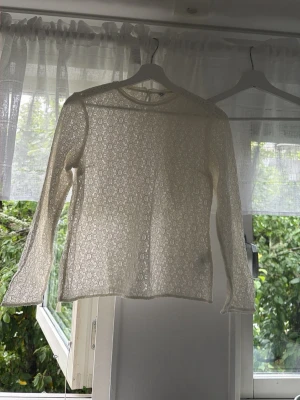 Vit spetsblus med lång ärm - Säljer en tunn, vit spetsblus med lång ärm och rund hals. Blusen har ett vackert spetsmönster. Perfekt för dig som gillar en feminin och stilren look.