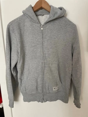Grå zip hoodie med huva - Säljer en enkel och stilren grå zip hoodie med huva och fickor framtill. Hoodien har dragkedja hela vägen och ribbade muddar vid ärmslut och nederkant🩶