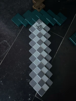 Minecraft-inspirerat svärd i plast med ljudeffekter  - Pixeligt svärd i grått och grönt, perfekt för cosplay eller maskerad. Tillverkat i plast med klassisk Minecraft-design och fyrkantiga former. Handtaget är mörkgrönt och bladet har olika grå nyanser. Med ljudeffekter.