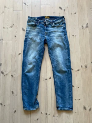 Blåa jeans - Jack & Jones  - Blåa jeans från Jack & Jones i storlek 30 32, modell: Tapered / Mike. Har några få defekter som syns på bild 5-7, små hål på benen och en fläck på högra benet. Annars fräscha. 