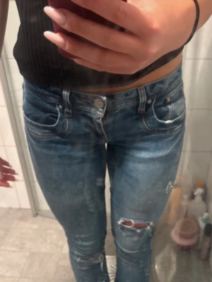 Blå slitna jeans med hål - Säljer ett par blå jeans med slitningar och hål på benen. Valerie 27/32!