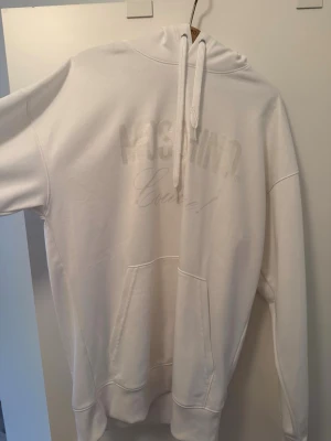 Vit hoodie från Moschino Couture - Säljer en clean vit hoodie från Moschino Couture med diskret logga framtill. Hoodien har stor huva med dragsko, magficka och ribbade muddar. Perfekt oversized fit och mjukt material som känns riktigt skönt mot huden.