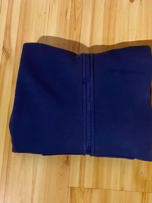 Mörkblå zip hoodie med fickor - En enkel och stilren mörkblå hoodie med dragkedja framtill och två stora fickor. Hoodien har en klassisk huva och ribbade muddar vid ärmar och nederkant. Perfekt för en avslappnad look och passar till det mesta.