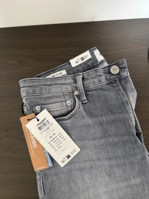 Grå regular jeans från Jack & Jones - HELT NYA! Snygga grå regula jeans från Jack & Jones med klassisk femficksmodell och bälteshällor. Jeansen har en ljus tvättad look och är tillverkade i ett mjukt, stretchigt material för extra komfort. Perfekta för en avslappnad och trendig stil.