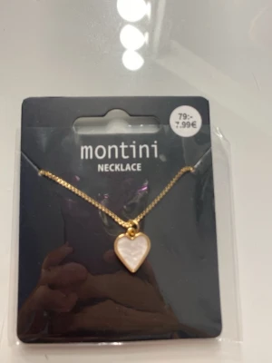 Halsband med hjärthänge  - Snyggt halsband från Montini med en guldfärgat kedja och ett hjärthänge i pärlemor-look. Hjärtat har en elegant guldkant och ger en trendig och söt vibe till din outfit. Perfekt accessoar för att lyfta din stil. 
