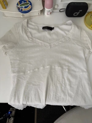 Vit blus med spets från KappAhl - Söt vit blus från KappAhl med v-ringning och spetsdetaljer runt halsen. Blusen har korta ärmar och diskret prickigt mönster upptill. Perfekt att styla med jeans eller kjol för en fräsch look. Luftig,