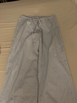 Randiga pyjamasbyxor i bomull - Ljusblå och vita vida pyjamasbyxor med tunna vertikala ränder och dragsko i midjan. 