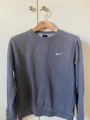 Grå sweatshirt från Nike - Klassisk grå sweatshirt från Nike med rund halsringning och diskret Nike-logga broderad på bröstet. Tröjan har långa ärmar och är tillverkad i mjuk bomullsblandning som är perfekt för en avslappnad stil.