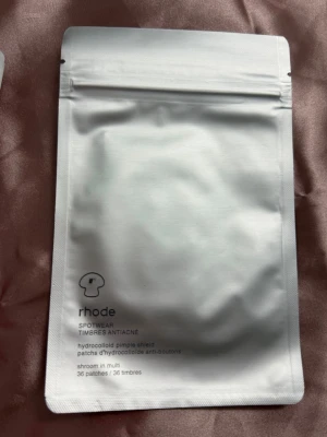 Rhode hydrocolloid pimple patches - Hydrokolloid plåster från Rhode, perfekta för att behandla finnar. Förpackningen innehåller 36 stycken plåster och har en stilren, vit design med tryckt text. Plåstren är diskreta och enkla att använda för punktbehandling.
