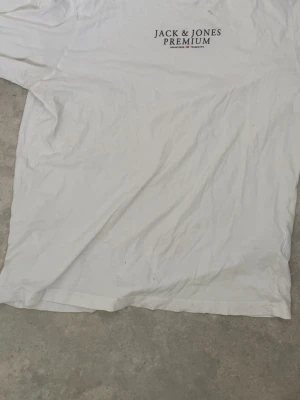 Vit t-shirt från Jack & Jones - Säljer en klassisk vit t-shirt från Jack & Jones Premium med tryck på bröstet. T-shirten har rund hals och korta ärmar. Perfekt basplagg till garderoben och enkel att matcha med olika stilar.