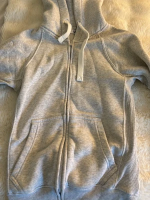 Ljusgrå zip-hoodie - russemerch - Ljusgrå hoodie med dragkedja, huva och tjocka vita snören. Köpt förra vintern och inte alls sliten eller några fläckar. Man kan köpa direkt för 325 💕