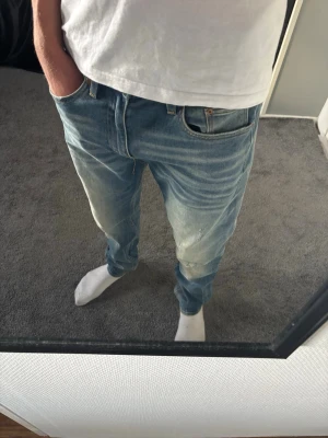 Straight leg jeans - Säljer ett par ljusblå jeans med raka ben och diskreta slitningar på framsidan. Jeansen har klassisk femficksdesign och är tillverkade i denim. Perfekta för en avslappnad och trendig look.