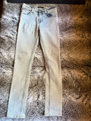 Nudie  - Ljusblå Nudie Jeans i storlek W27/L32, i smal modell med mörka broderier på bakfickorna.