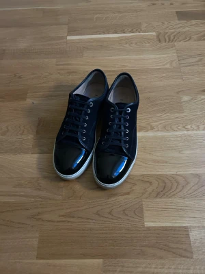 Mörkblåa lanvin skor - Snygga svarta sneakers med glansiga lackdetaljer på tån och klassisk vit sula. Skorna har svarta skosnören och silverfärgade öljetter. Perfekta för dig som vill ha en stilren men ändå trendig look. Storlek 46