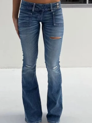 Blå bootcut jeans - Snygga blå bootcut jeans med slitningar på låret och knäna. Jeansen har hög midja, raka ben som blir vidare nedtill och stora fickor framtill. Perfekta för en avslappnad och trendig look.