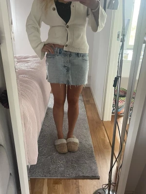 Ljusblå jeanskjol med rå kant - Trendig ljusblå jeanskjol i kort modell med rå, fransig kant nertill. Klassisk femficksdesign och dragkedja framtill. Perfekt för en avslappnad och cool stil.