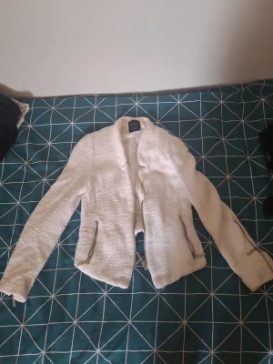Vit jacka från Zara Trafaluc - Säljer en snygg vit jacka från Zara Trafaluc. Jackan har en strukturerad yta, dragkedjor vid fickorna och ärmarna samt en öppen front. Perfekt för dig som vill ha en stilren och trendig look.
