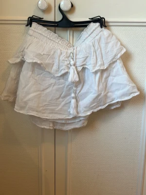Vit kjol Gina Tricot - Söt vit kjol från Gina Tricot med volang och snörning med tofsar framtill. Kjolen har flexibla resår upptill och är gjord i ett tunt, luftigt tyg som passar perfekt till sommaren. Priset går att diskutera. Säljer för att den är för liten för mig! 