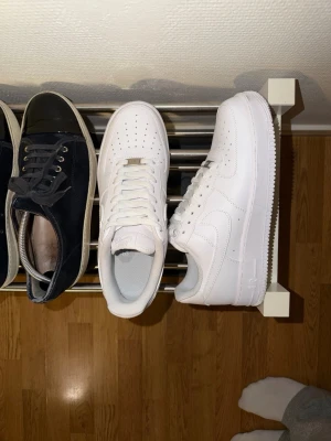 Nike Air Force 1  - Klassiska Nike Air Force 1 sneakers i helvitt läder med perforerad tåbox, vita skosnören och den ikoniska swoosh-loggan på sidan. Tjock sula med mönster för bra grepp. Perfekta för en clean och stilren look. Skulle säga att dem passar mer 43 än 42.5. Tycker dem är stora i storleken