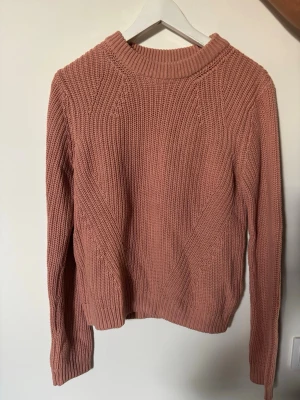 Rosa stickad tröja från H&M - Mysig stickad tröja från H&M i en mjuk rosa färg. Tröjan har rund halsringning, ribbade muddar och ett snyggt stickat mönster. Perfekt för kyliga dagar och enkel att matcha med jeans eller kjol.