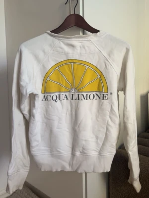 Vit sweatshirt Acqua Limone citron - Vit sweatshirt med stort gult citrontryck och Acqua Limone-logga på bröstet. Tröjan har rund halsringning, långa ärmar och ribbade muddar. Perfekt för en avslappnad och trendig stil. Den är använd många gånger därför har den några defekter. Sjukt snygg med citronen på ryggen! 700 kr nypris så jag vill inte gå under 150kr