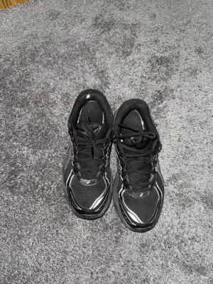 Asics gt-2160 - Säljer ett par svarta Asics-sneakers med silvriga detaljer. De har ett litet hål i hälfodret på vänster sko, men är i övrigt i gott skick och redo att användas. 