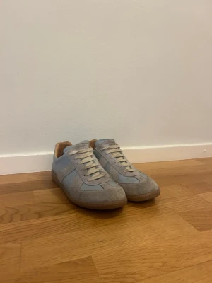 Ljusgrå sneakers i mocka och läder - Snygga ljusgrå sneakers med ovandel i mocka och läderdetaljer. Skorna har vita snören och en klassisk gummisula i brunt. Insidan är fodrad i beige textil för extra komfort. Perfekta för en clean och stilren look.