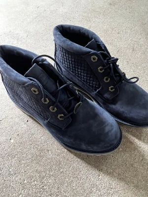 Mörkblå Timberland kängor - Säljer ett par mörkblå Timberland kängor i mocka med quiltade detaljer på sidorna och robust sula. Kängorna har metallöljetter och klassisk snörning. Perfekta för dig som vill ha en stilren och tålig sko till hösten och vintern. De är i strl 38 men sitter väldigt små så skulle säga att de passar mest 37. Sparsamt använda ett fåtal gånger.