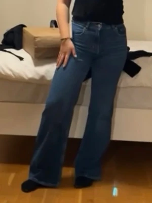 Blåa utsvängda jeans med hög midja - Säljer ett par blåa jeans med hög midja och utsvängda ben. Jeansen har klassisk femficksdesign och stängs med dragkedja och knapp. Perfekta för dig som gillar en retro och avslappnad look. Skriv för bättre bilder
