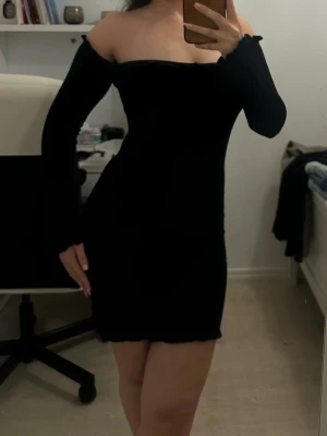 Svart offshoulder kort klänning - Säljer en svart, tight offshoulder klänning med lång ärm och stretchigmaterial. Klänningen är kort och har en enkel, stilren design som framhäver figuren. 