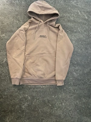 Beige hoodie med tryck Daily Essentials - Tja! Säljer min ljusbruna new yorker tröja med tryck på båda baksidan och framsidan ”Daily Essentials” 