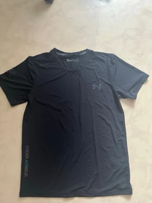 Svart träningsset från Under Armour - Säljer ett svart träningsset från Under Armour med en kortärmad t-shirt och matchande shorts. Båda plaggen har diskreta loggor och är tillverkade i ett lätt, snabbtorkande funktionsmaterial som passar perfekt till gymmet eller löpning.