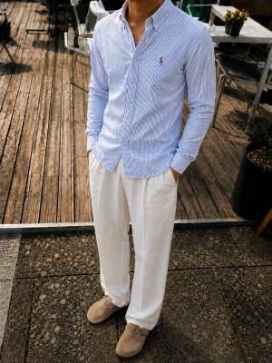 Polo Ralph Lauren Slim Fit Skjorta – Blå/Vit Randig – Stl S - Snygg Polo Ralph Lauren Slim Fit skjorta i klassiskt blå- och vitrandigt mönster. Skjortan har den ikoniska broderade Polo-spelaren på bröstet och en stilren button-down-krage.  * Modell: Slim Fit * Storlek: S * Färg: Ljusblå / vit * Klassisk randig struktur * Broderad Polo Ralph Lauren-logga * Button-down-krage * Långärmad * Perfekt till jeans, chinos eller ljusa linnebyxor  En stilren och lättmatchad skjorta som passar perfekt till en preppy / old money look.