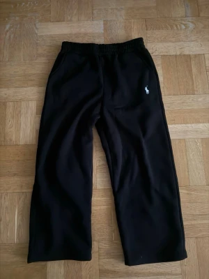 Svarta mjukisbyxor från Polo Ralph Lauren - Svarta mjukisbyxor med resår i midjan och raka ben. Byxorna har två sidofickor och en vit broderad Polo Ralph Lauren-logga på vänster sida. Perfekta för en avslappnad och stilren look.