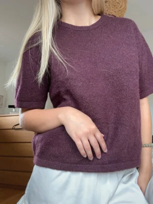 Kortärmad vinröd stickad tröja - Mysig vinröd stickad tröja med korta ärmar och rund hals. Tröjan har en rak passform och är tillverkad i ett mjukt, luddigt material som känns skönt mot huden. Perfekt att styla med både jeans och kjol för en avslappnad look.
