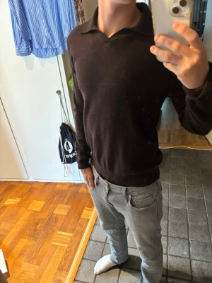 Brun merino ull polo - Stilren brun långärmad tröja med klassisk krage. Tröjan har en enkel och clean design utan synliga loggor eller mönster. Perfekt till jeans eller chinos för en avslappnad men snygg look. Materialet ser ut att vara mjukt och stretchigt.