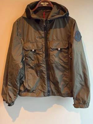Olivgrön Moncler vindjacka/windbreaker  - Denna Moncler jacka är ÄKTA, då bevis även finns på bilderna. Säljer denna riktigt feta vindjacka då den blivit för liten. Den är perfekt nu när kylan börjar komma. Den ända ’’skadan’’ vad jag vet är att några sömmar på märket lossnat, men det kan fixas lätt👍. Jackan är i storlek XS men kan även passa S.