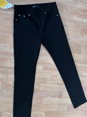 Svarta  jeans med hög midja - Snygga svarta  jeans med hög midja och klassisk femficksdesign. Jeansen har smala ben och kopparfärgade nitar vid fickorna. Perfekta för en trendig och stilren look. Materialet känns stretchigt och bekvämt.