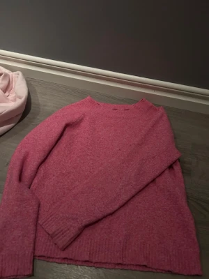Rosa stickad tröja från Vero Moda - Mysig rosa stickad tröja från Vero Moda i storlek XS. Tröjan har rund halsringning, långa ärmar och ribbstickade muddar vid ärmslut och nederkant. Perfekt för att hålla värmen under kyliga dagar.