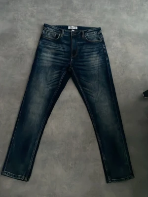 Mörkblå slim fit jeans med slitningar - Snygga mörkblå jeans i slim fit-modell med tydliga slitningar och tvättade detaljer på framsidan. Klassisk femficksdesign, bälteshällor och dragkedjegylf. Perfekta för en trendig och avslappnad stil.