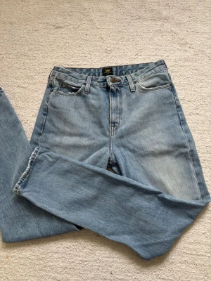 Ljusblå mom jeans från Lee - Säljer ett par ljusblå mom jeans från Lee med rak passform och hög midja. Klassisk femficksmodell i mjukt denimtyg. Perfekta för dig som gillar vintage vibe och avslappnad stil.