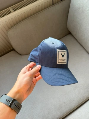 Callaway Golf Flexfit keps – blå - Snygg golfkeps från Callaway i mörkblå färg med klassisk Callaway-patch framtill. Flexfit-konstruktion och justerbar snapback baktill för bra passform.  Tillverkad i lätt och ventilerande funktionsmaterial, perfekt för golfbanan men även snygg till vardags.  Fint begagnat skick, se bilder.  