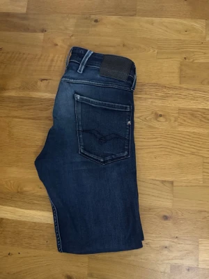 Mörkblå jeans från Replay 31/30 - Snygga mörkblå jeans från Replay med klassisk femficksmodell och diskreta slitningar. Jeansen har raka ben och detaljerade sömmar på bakfickan. Perfekta för en avslappnad och trendig stil. OBS! (liten defekt på en av skärp öglorna men går lätt att sy tillbaks se på bild 4) 